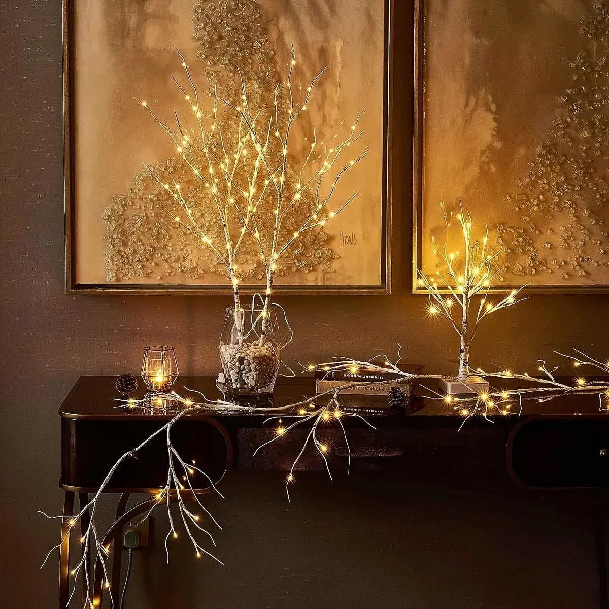 LED Illumination BrightBranch - Yelopi - Three Birch Treest with LED light on, 2 inside a vase and 1 standalone, on a table, sided by decorative frames.