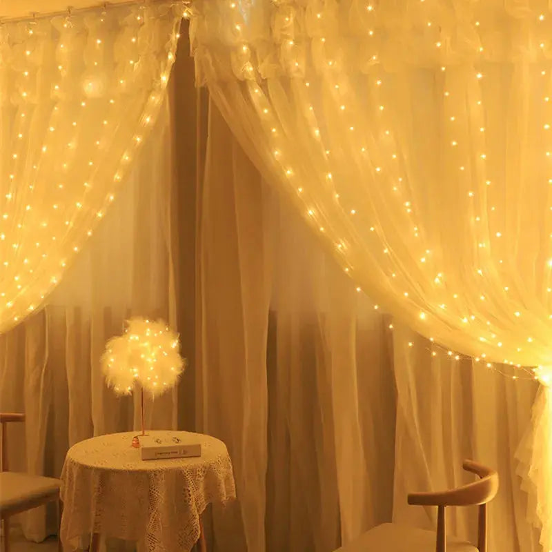 TwinkleVeil LED Drapes - Yelopi - Warm color, lights on, in a living room window, sided by a small table and two chairs.